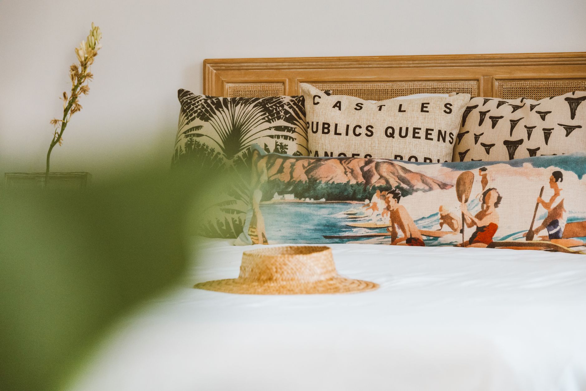 A stylish bed with artistic pillows and a straw hat exuding a relaxed, summer vibe.